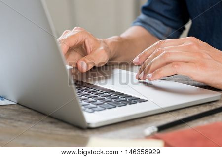 Closeup hand of businessman using laptop at office. Close up view of man hands working on laptop while sitting at wooden desk. Closeup of casaul worker typing on laptop computer and surfing internet.