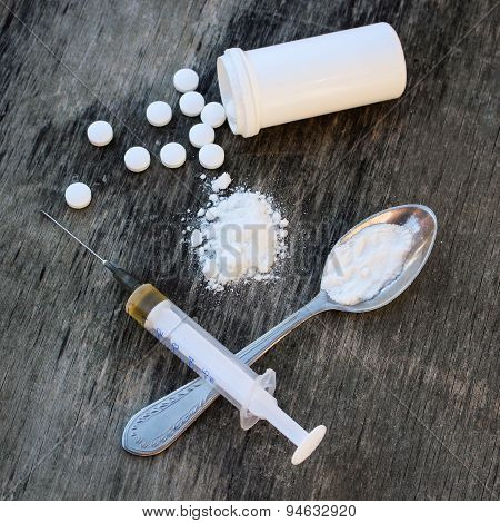 White pill, syringe and heroin on spoon on the old wooden background. Drug addiction.