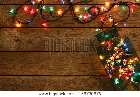 Christmas lights background. Holiday shiny garland border spread from glass jar, top view on brown wooden planks surface. Xmas tree decorations, winter holidays illumination