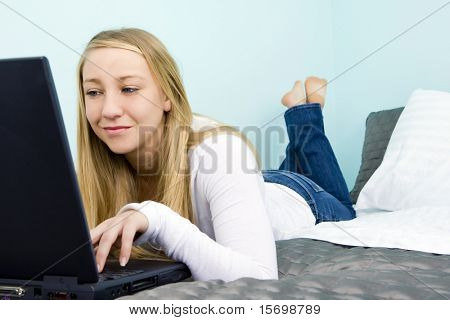 Teen girl laying on her bed looking on her laptop