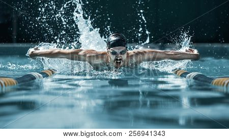 The Dynamic And Fit Swimmer In Cap Breathing Performing The Butterfly Stroke At Pool. The Young Man.