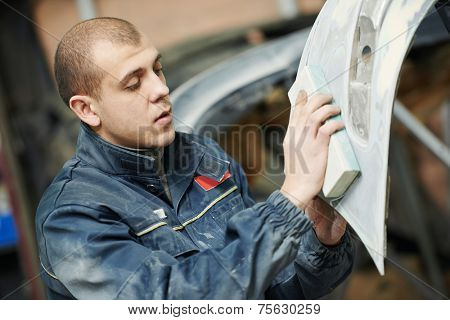 auto mechanic worker sanding polishing bumper car at automobile repair and renew service station shop by sandpaper