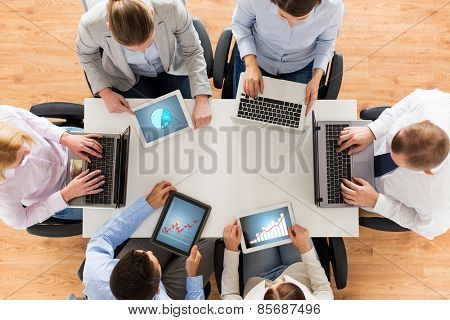 business, people and technology concept - close up of creative team with laptop and tablet pc computers displaying charts on screens sitting at table in office