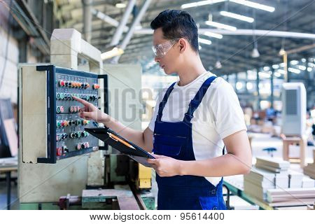 Worker pressing buttons on CNC machine control board in Asian factory