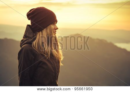 Young Woman standing alone outdoor with sunset mountains on background