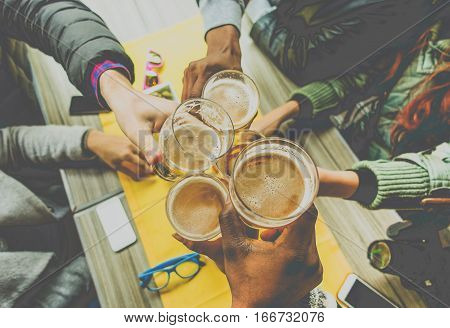 Top view of friends cheering with home brew in pub bar restaurant - Young people hands toasting and beers half pint - Friendship and party concept - Warm matte filter - Focus on bottom hand