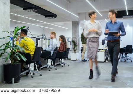 Group of businesspeople working in creative office. Interior of busy employees in a co-working space. Corporate businessmen and businesswomen sitting at desks and walking at work.