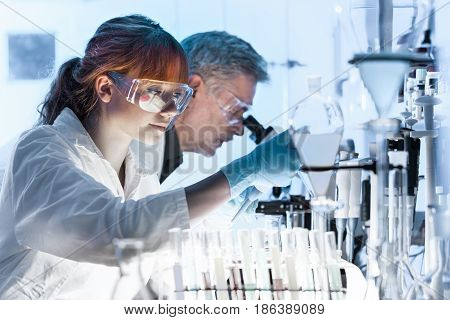 Health care researchers working in life science laboratory. Young female research scientist and senior male supervisor preparing and analyzing microscope slides in research lab.