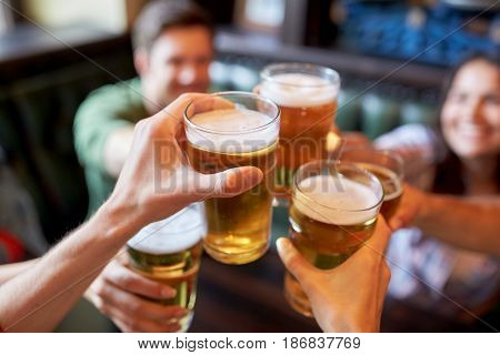 people, leisure, friendship and celebration concept - happy friends drinking draft beer and clinking glasses at bar or pub