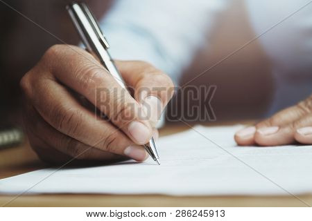 Hand Of Woman Holding Pen With Writing On Paper Report In Office