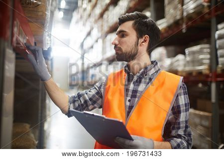 Side view portrait of bearded warehouse worker checking labels on shelves with goods while doing inventory controlWarehouse worker reviewing goods