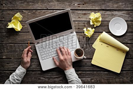 Laptop with blank notepad and pencil with sheets of crumpled paper on old wooden table. Top view of workplace writer.