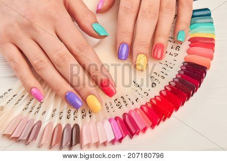 Summer manicure and nail color samples. Young woman hands with multicolored manicure and collection of color nail polish samples. Nail beauty salon.