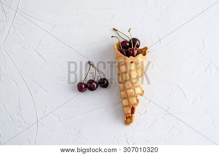 Ice Cream Cone Filled With Cherries On A Light White Concrete Background.