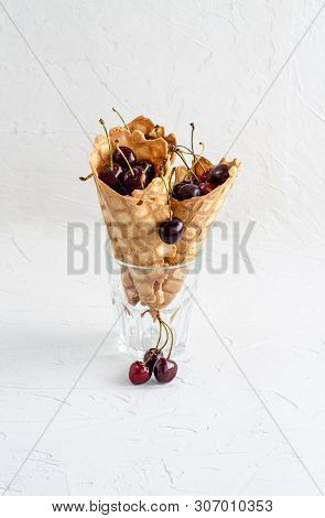 Three Ice Cream Cones Filled With Cherries In A Glass Beaker On A Light White Concrete Background.