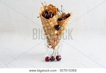 Three Ice Cream Cones Filled With Cherries In A Glass Beaker On A Light White Concrete Background.