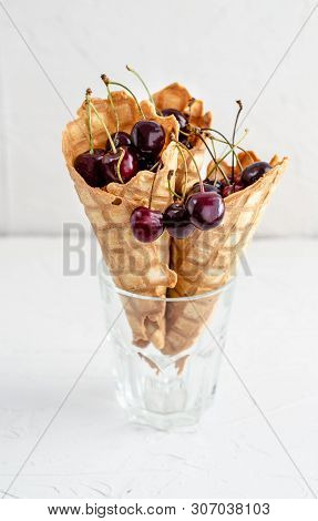 Three Ice Cream Cones Filled With Cherries In A Glass Beaker On A Light White Concrete Background.