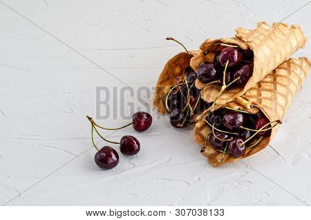 Ice Cream Cone Filled With Cherries On A Light White Concrete Background.