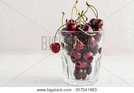 Ripe Fresh Red Sweet Cherry In A Glass Beaker On A White Concrete Background