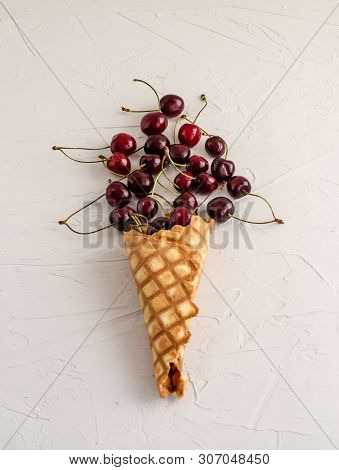 Ice Cream Cone Filled With Cherries On A Light White Concrete Background.