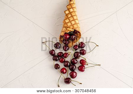 Ice Cream Cone Filled With Cherries On A Light White Concrete Background.