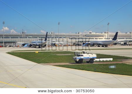 Armored police vehicle secures perimeter and exit to runway and two passenger airliners on the background standing at the gates in Munich International Airport, Germany.