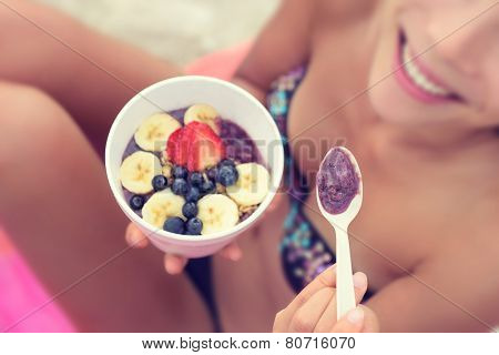 Acai bowl - girl eating healthy food on beach. Woman enjoying acai bowls made from acai berries and fruits outdoors on beach for breakfast. Girl on Hawaii eating local Hawaiian dish.