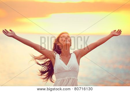 Free happy woman arms up praising freedom at beach sunset. Young adult enjoying breathing freely fresh air.