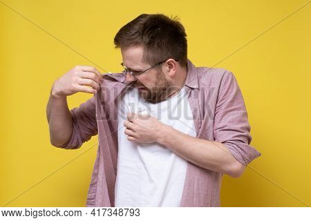 Disgruntled Man With Glasses And Casual Clothes Sniffs His Armpits, Annoyed By The Problem Of Sweat 