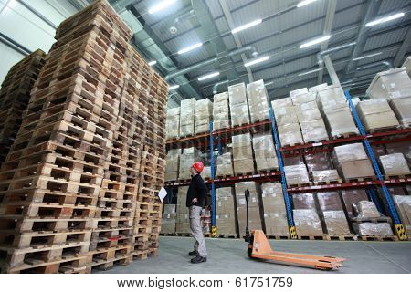 stack of wooden pallets in storehouse - 	worker with hand pallet truck preparing delivery