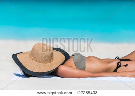 Beach relaxation woman sleeping sun tanning covering her face with straw hat for uv solar protection on caribbean destination blue ocean background. Vacation girl relaxing resting on summer travel. 