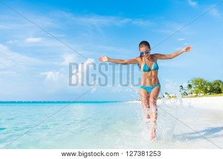 Freedom carefree girl playing splashing water having fun on tropical beach vacation getaway travel holiday destination. Playful woman with abs slim bikini body relaxing feeling free. 