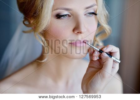 Wedding makeup artist making a make up for bride. Beautiful sexy model girl indoors. Beauty woman with curly hair. Female portrait. Bridal morning of a cute lady. Close-up hands near face