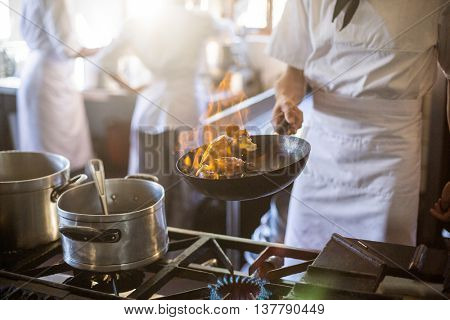 Mid section of chef tossing stir fry over large flame in commercial kitchen