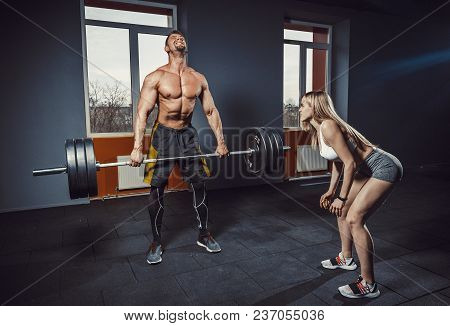 Fit Woman Motivates Man While He Doing Deadlift With Heavy Barbell. Man Lifting Barbell Opposite Win