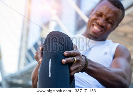 African American Male Runner Bends Over Clutching His Knee While In Intense Pain From An Acute Knee 