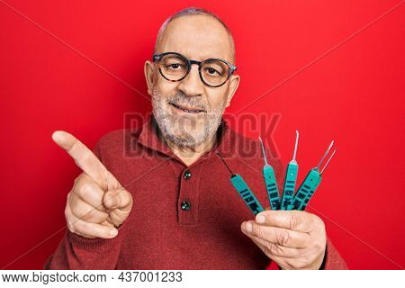 Handsome mature man holding picklock to unlock security door smiling happy pointing with hand and finger to the side 