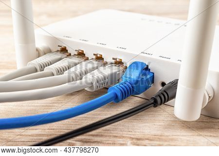 Blue And Gray Network Cable Plugs Connected To The White Wi-fi Wireless Router On A Wooden Desk. Clo