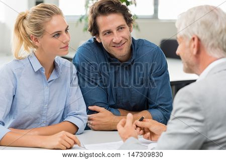 Businessman explaining loan policy to young couple. Happy couple discussing with a financial agent their new investment. Financial consultant presents bank investments to a smiling woman and her man.