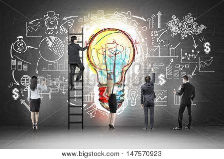 Rear view of business team near blackboard with colorful light bulb and startup sketch drawn on it. Concept of idea of business