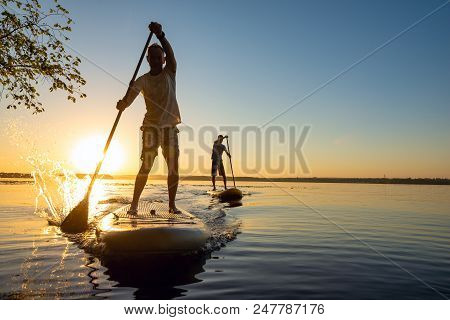 Men, Friends Sail On A Sup Boards In A Rays Of Rising Sun. Stand Up Paddle Boarding - Awesome Active