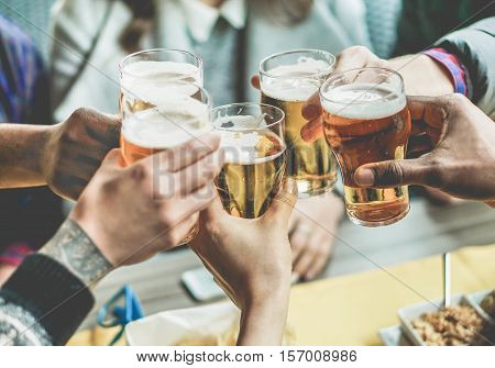 Multiracial group of friends enjoying a beer - Young people hands toasting and cheering aperitif beers half pint - Friendship and youth concept - Warm vintage filter - Focus on bottom hand