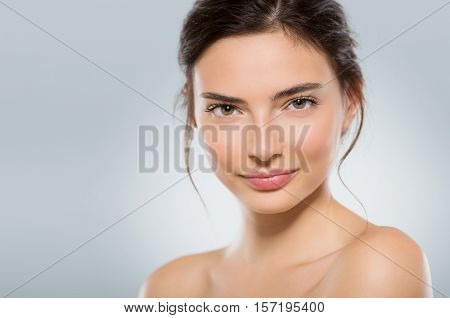 Beautiful face of a young woman with clean fresh skin isolated on light blue background. Close up face of natural gil after beauty treatment looking at camera. Skincare and body care concept.