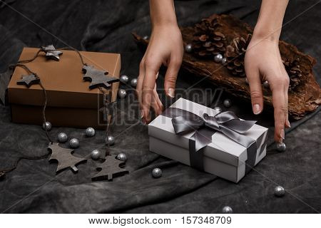 Girl's hands put gift box on table. Christmas decoration over grey background.