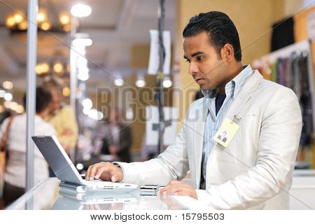 Joven empresario indio usando la computadora portátil en la feria.