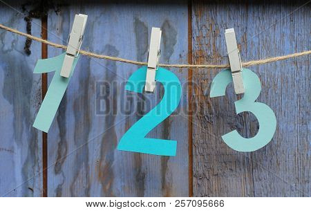 The Numbers One, Two And Three  Cut From Paper And Pegged Onto String In Front Of Rustic Painted Woo