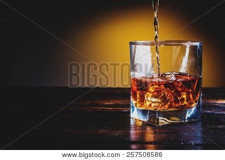 Alcohol Drink Whisky, Whiskey Or Bourbon With Ice Cubes On Dark Wood Table And Orange Background