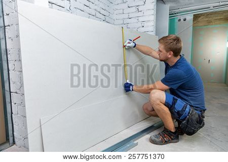 Man Measuring Plasterboard Sheet For Interior Construction