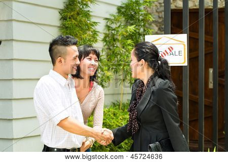 Real estate market - young Indonesian couple looking for real estate apartment or house to rent or buy, the realtor and the client shaking hands	