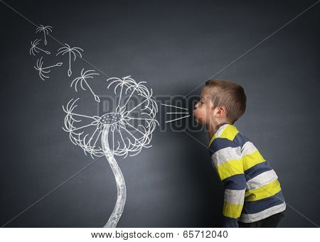 Child blowing dandelion seeds on a blackboard concept for wishing, hope and aspirations